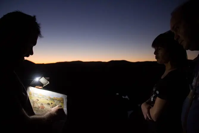 Marco showing an illustration to visitors at sunset